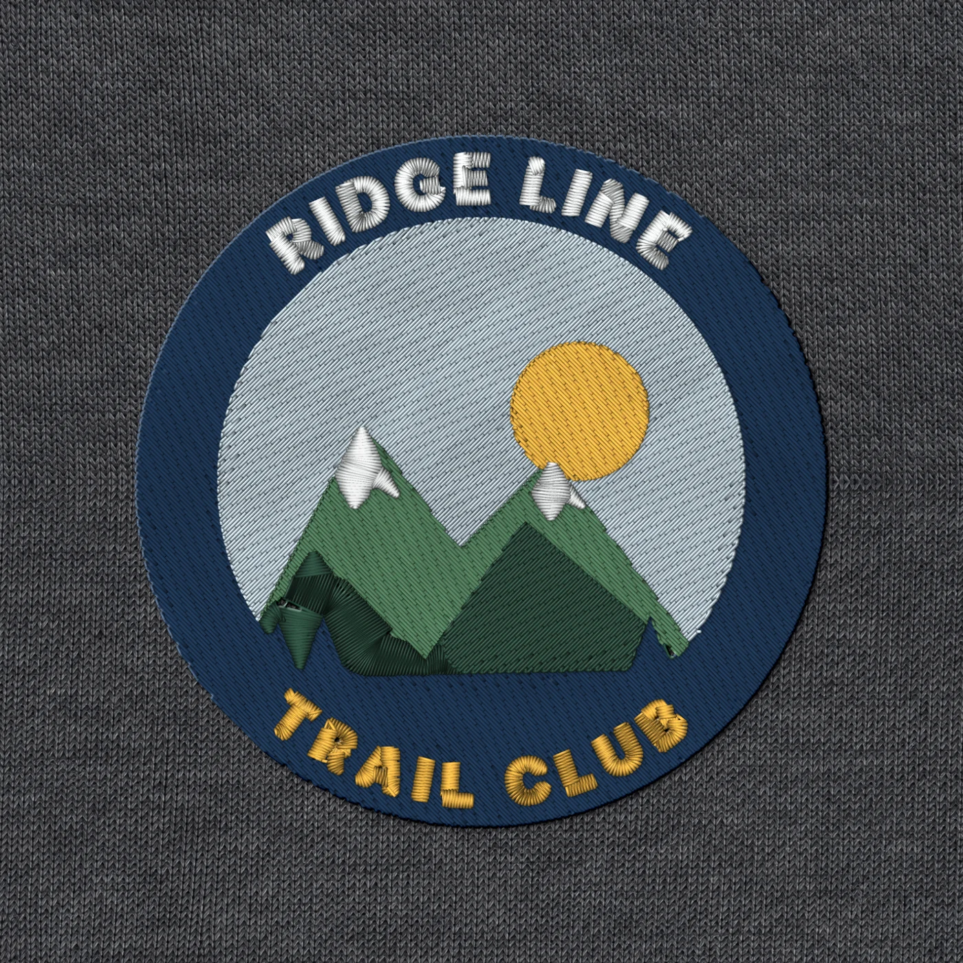 Stitched render on fabric of a round patch: green fill mountains and a gold sun inside a navy satin ring with arched lettering
